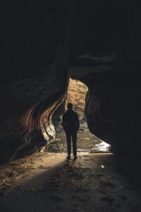 Emerging Into the Light A person stands at the entrance of a rugged cave, silhouetted against the bright light outside, symbolizing the transition from uncertainty to clarity, embracing personal growth beyond comparison.