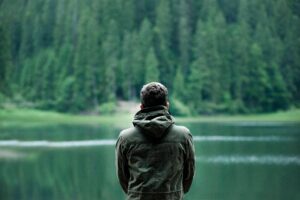 Reflecting on self-worth and clarity in nature's silence A person standing alone by a calm forest lake, reflecting on life and inner peace